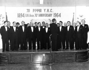 Group of men in tuxedos preparing to perform a song at the 1964 UNA 70th Anniversary